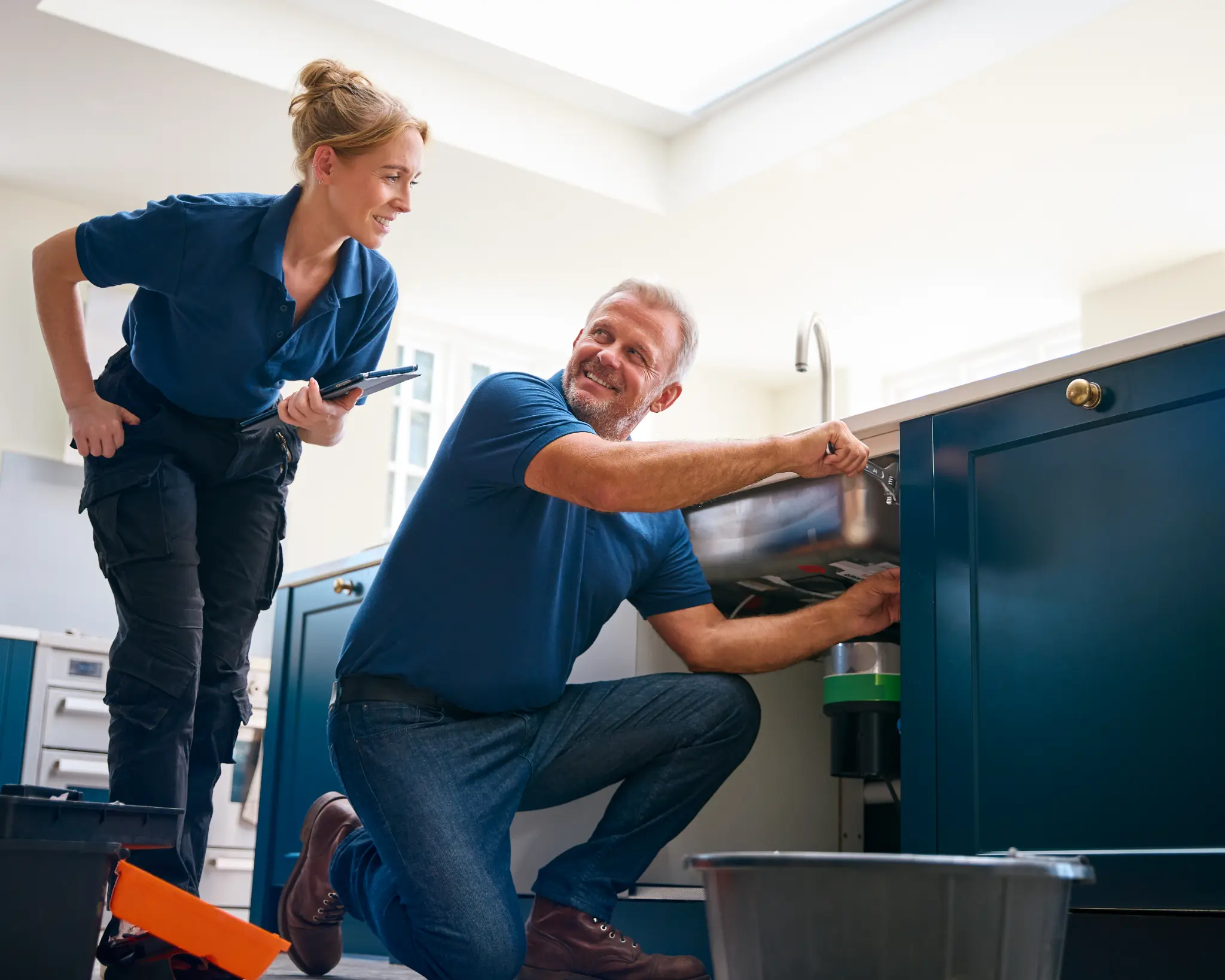 Two plumbing professionals coordinating beside an open kitchen sink with a digital tablet