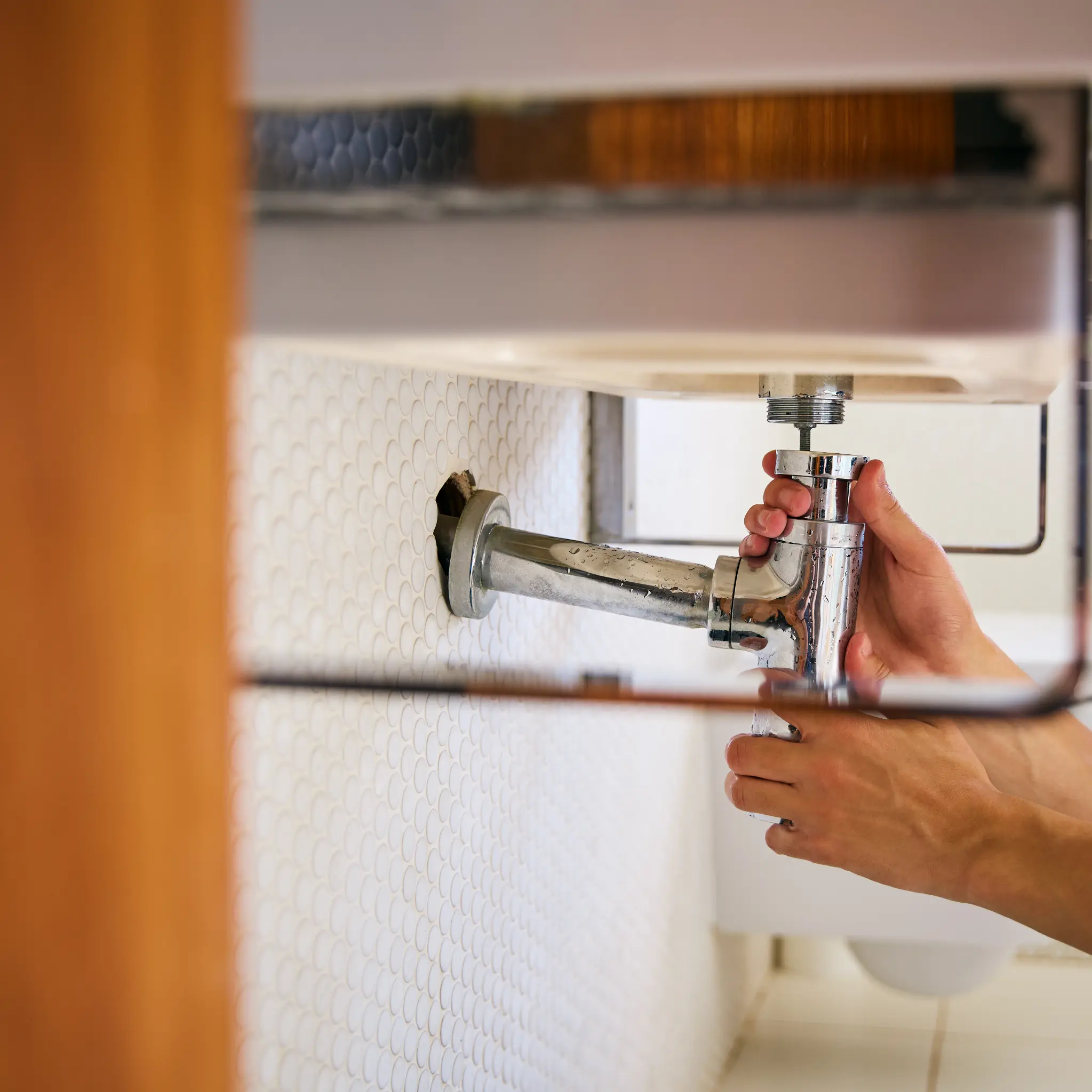 Close-up of a plumber adjusting the chrome drain trap beneath a bathroom sink