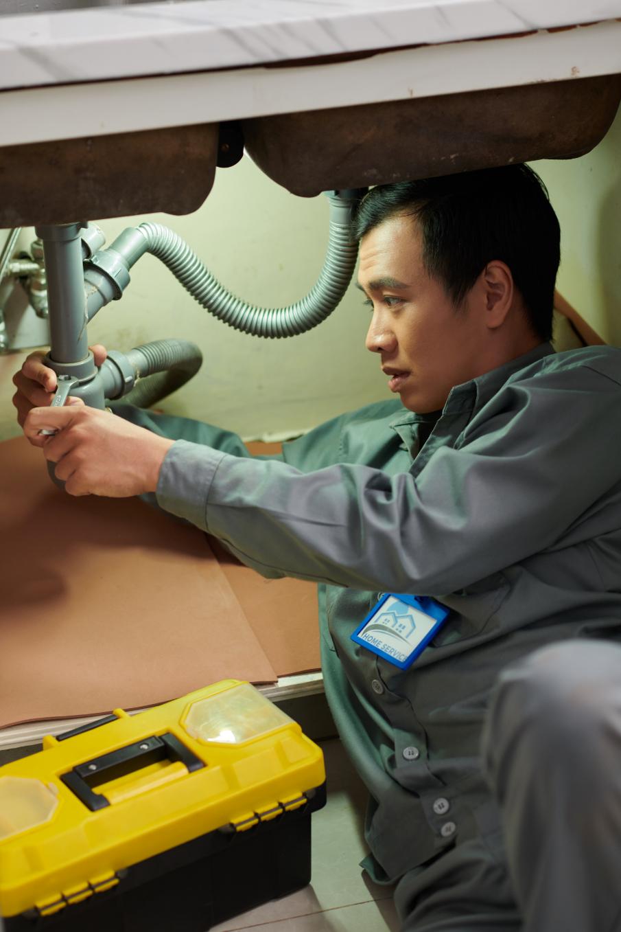 Plumber loosening a slip nut on the drain pipe beneath a sink