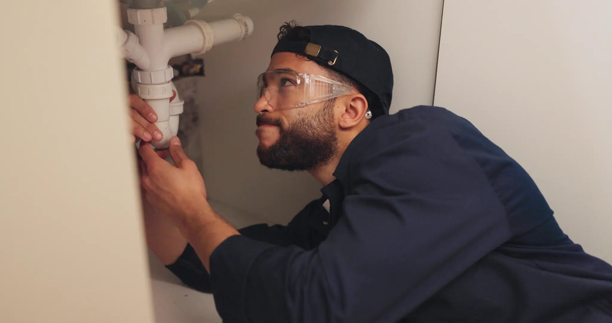 Plumber inspecting a white drain trap beneath a kitchen sink