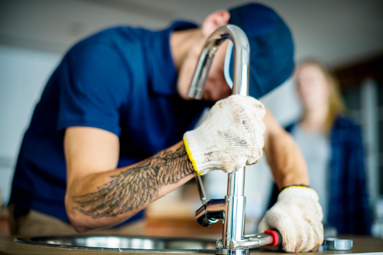 Gloved plumber tightening a chrome kitchen sink faucet with a wrench