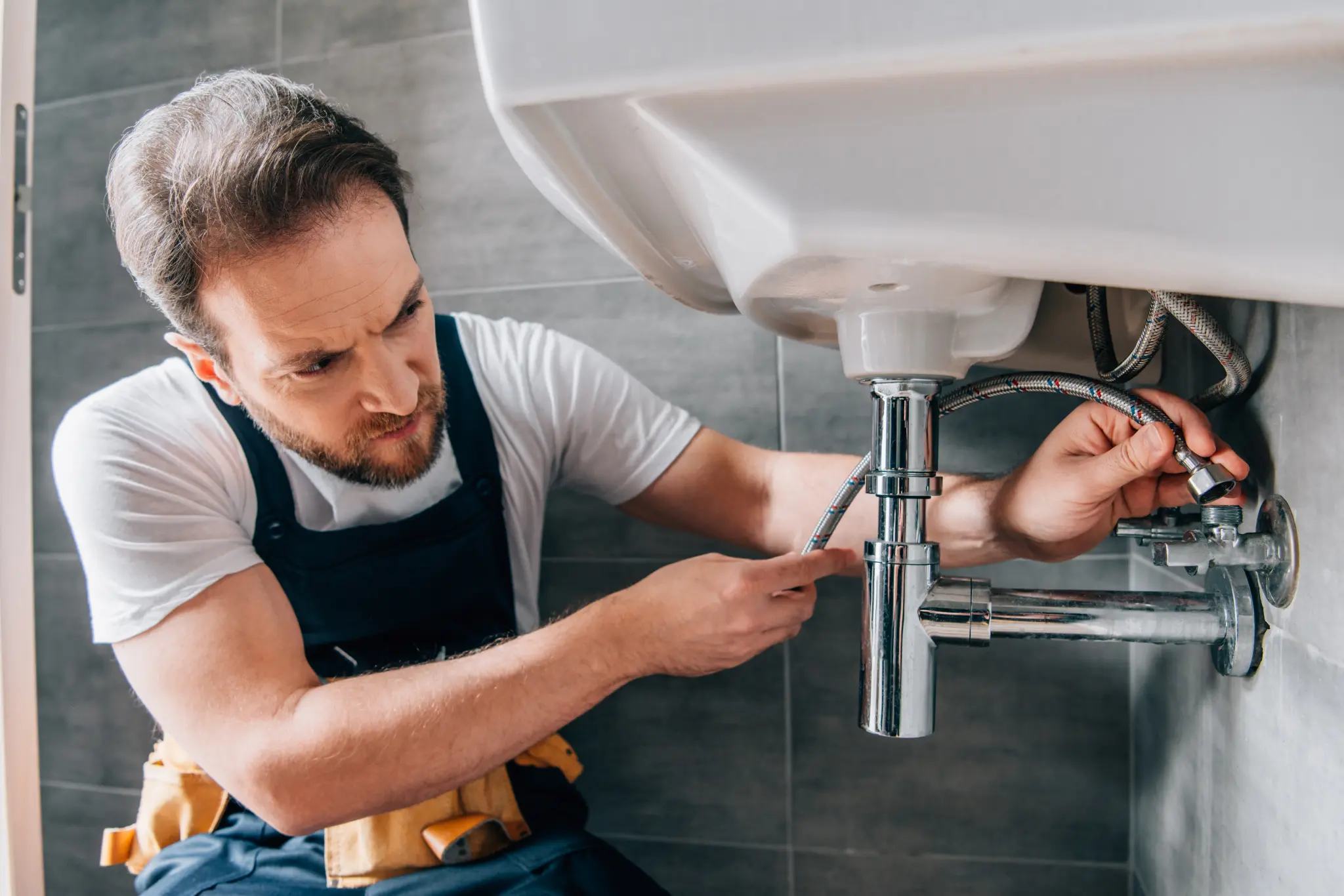 Plumber working on braided water supply lines beneath a bathroom sink